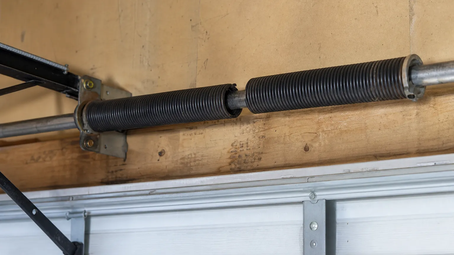 Broken torsion spring with a visible gap in the coil on a steel shaft above a garage door