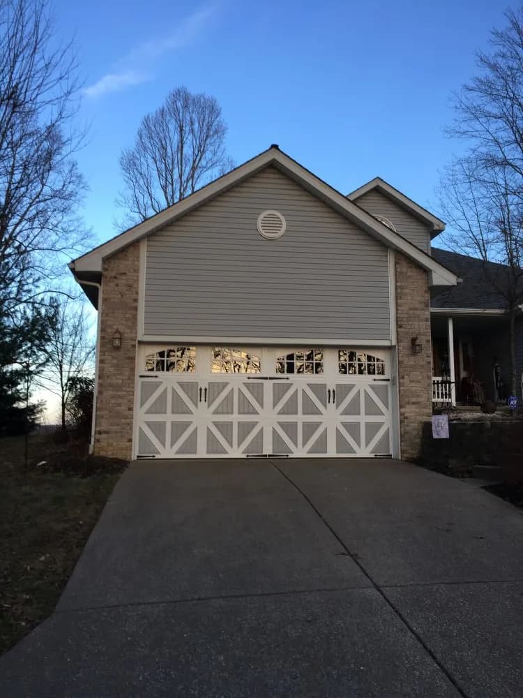 White carriage style garage door with arched windows on a brick and grey siding home