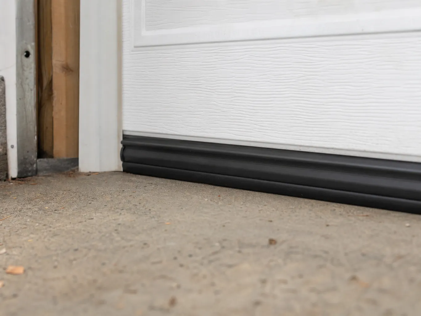 Bottom edge of a white garage door meeting the concrete floor with a new rubber weather seal